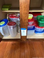 Storage containers with lids in various colors including red, green, blue, and yellow, stacked inside a wooden cabinet.