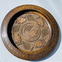 Full view of the carved wood charger plate showing detailed grape clusters and leaf carvings with geometric patterned border.