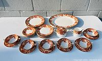 Top-down view of entire set showing arrangement of large platter, various plates, bowls, cream pitcher, and sugar bowl with rust floral pattern.