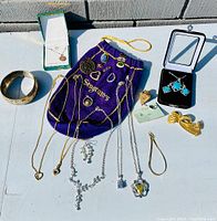 Photo shows entire assortment of estate jewelry including necklaces, earrings, rings, pins, gold-tone bangle and bow-shaped clip, turquoise earrings in black box, all laid on a white surface with purple Seagram's pouch.