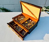 Wide shot of open velvet-lined jewelry box showing assorted costume jewelry inside compartments and drawer