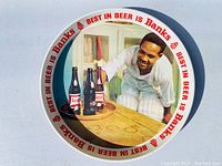 Top-down view of round metal serving tray featuring vintage Banks Beer advertising with a man reaching for bottles of beer.