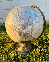 Front view of vintage globe showing Asia and surrounding regions with silver tone base in grass.