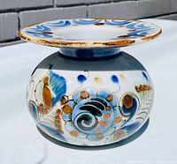 Side angle of the pottery vase displaying hand-painted blue and brown abstract floral designs with a wide flared rim.