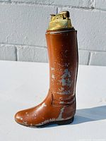 Front left angled view of the vintage boot shaped lighter showing paint wear and brass lighter mechanism.