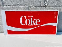 Front view of rectangular Coca Cola metal sign with red and white color scheme showing 'Drink Coke' text and some wear.