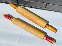 Two vintage wooden rolling pins, one with original red painted handles and the other with natural wood handles.
