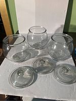 Three clear round glass jars with detached lids arranged on a white surface.