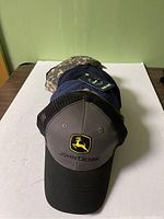 Front view of hats stacked with John Deere cap on top showing logo and mesh back