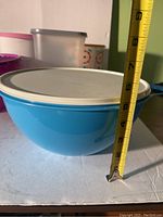 Side view of large blue Tupperware container with white lid and measuring tape next to it showing approximately 5 inch height