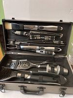 Overview of the grill set inside the carrying case including spatula, fork, tongs, basting brush, and skewer neatly organized