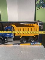 Photo showing the left side of the Bruder Mack dump truck toy inside original box, with measuring tape indicating approximately 20 inches length