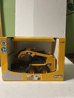 Front view of Bruder CAT skid steer loader toy in yellow packaging showing full loader and bucket.