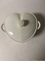 Top view of heart-shaped white cast iron Dutch oven lid with heart-shaped handle embossed with 'WELL EQUIPPED KITCHEN'