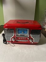 Front view of red Crosley alarm clock radio showing analog clock face, chrome accents, dials, and buttons.