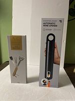 Box of Sharper Image Automatic Wine Opener and Modern Expressions 5-in-1 BBQ Tool standing side by side.