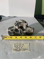 Photo showing front of lava rock with calcite and quartz crystal cavity, approximately 7 inches wide, with measuring tape for scale and handwritten label.