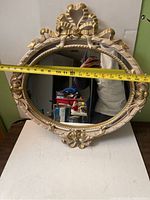 Oval ornate wall mirror with gold-colored carved frame showing width measurement of approximately 22 inches