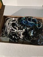 Over 40 assorted beaded costume necklaces in a box, showing a mix of clear, white, black, and blue beads.