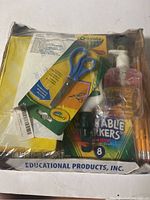 Top view of box with Crayola scissors pack, crayons, washable markers, pencils, hand sanitizer, and pencil sharpeners visible inside the box with plastic wrap.