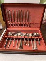Wide view of the entire silverware set inside the wooden case with reddish-orange lining.