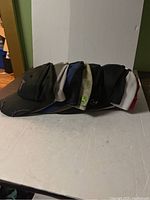 Side view of the 9 assorted hats stacked side by side showing various colors and designs