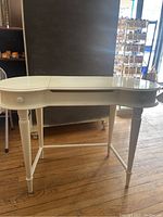 Front view of white makeup vanity showing curved top, two drawers, turned legs and cross bars.