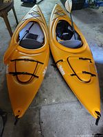 Two orange kayaks side by side with paddles in cockpits and deck bungee rigging visible
