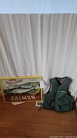 Photo of the entire set showing the fishing vest and canvas salmon print side by side on wood floor with white curtain backdrop.