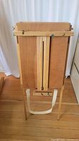 Rear view of wooden easel showing folding legs, straps and easel back panel with clasps.