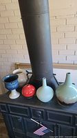 Overview of all five pottery pieces showing varying shapes, heights, and colors placed on a black surface with a wood stove in the background.