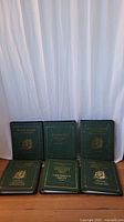 Six green hardcover binders arranged on floor to show front covers with gold embossed titles and emblems.