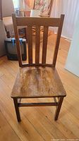 Front view of the wooden chair showing the straight back with three vertical slats and worn seat surface.