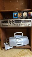 Panasonic AM/FM stereo receiver with 8 track player on upper shelf, 4 ABBA 8 track tapes behind it, and Aiwa portable CD/cassette/AM/FM stereo below in wooden shelving.