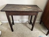 Front view of antique solid wood side table against white wall, showing rectangular top, four straight legs, and apron with missing drawer used inverted.