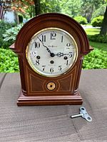 Full front view of Howard Miller mantel clock on outdoor surface with winding key visible