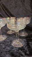 Four iridescent molded champagne coupe glasses arranged on black fabric with visible Art Deco style and iridescent finish.