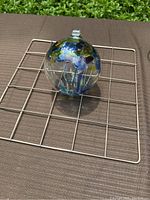 Kitras art glass ball photographed on a wire rack outdoors, showing round clear glass surface and colorful internal glass design.