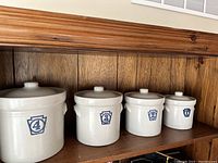 Photo showing front view of the four Pfaltzgraff Yorktowne canisters, cream color with blue numbered keystone lids from numbers 4 to 1 left to right.