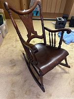 Full view of one antique solid wood rocking chair showing the curved high back with mother of pearl inlay, armrests, and curved seat.