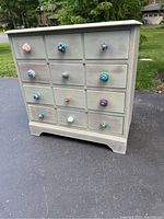 Front view of the small chest of drawers with all drawers and colorful ceramic knobs visible, showing the painted distressed finish and overall condition.