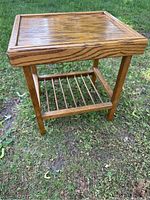 Full view of the solid wood side table standing on grass showing top and shelf