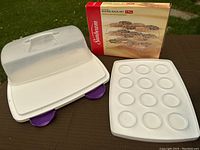 Wilton plastic cupcake and cake carrier with locking translucent lid and purple latches, shown with Sunbeam 3-piece stackable baking rack set box