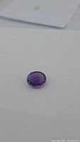 Photo showing deep purple oval cut amethyst gemstone on white background