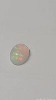 Close-up photo of the oval cabochon Ethiopian opal showing multicolored flashes on a white background.