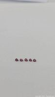 Five small pear-shaped blood red rubies lined up horizontally on a white background.