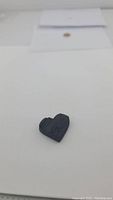 Small, hand carved black tourmaline in heart shape shown from one angle, highlighting the textured surface and terminated crystal edges.