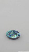 Oval natural abalone doublet cabochon gemstone, showing swirling iridescent colors with predominant blue and green tones.