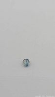 Close-up image of an oval cut natural blue sapphire gemstone showing light bicolor off-white and teal blue coloration on white background.