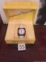 Watch in its original yellow Invicta box placed on a wooden surface showing some wear on the box